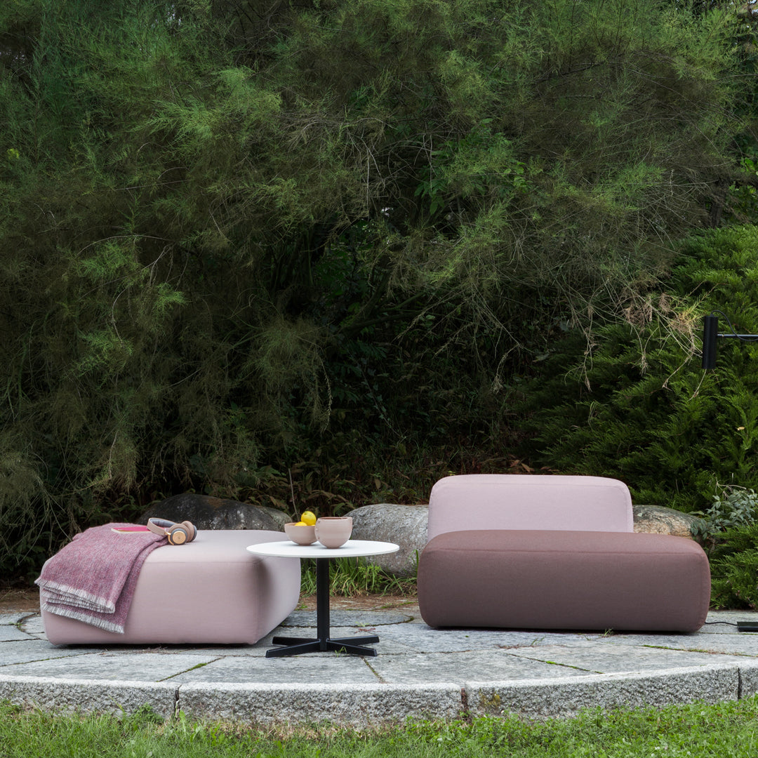 Two contemporary outdoor chairs in soft pink and brown, paired with a minimalist black table on a stone patio.