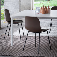 Brown chairs with black legs on a textured light gray woven rug, paired with a minimalist white table and pastel ceramic vases.