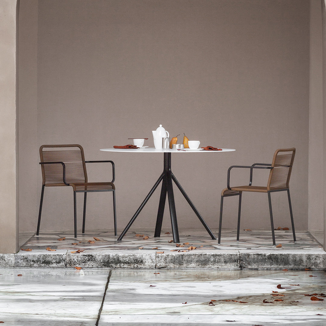 Modern round table with white surface and brown woven chairs against a muted beige backdrop, complemented by soft earth tones.