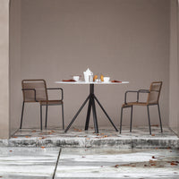 Modern round table with white surface and brown woven chairs against a muted beige backdrop, complemented by soft earth tones.