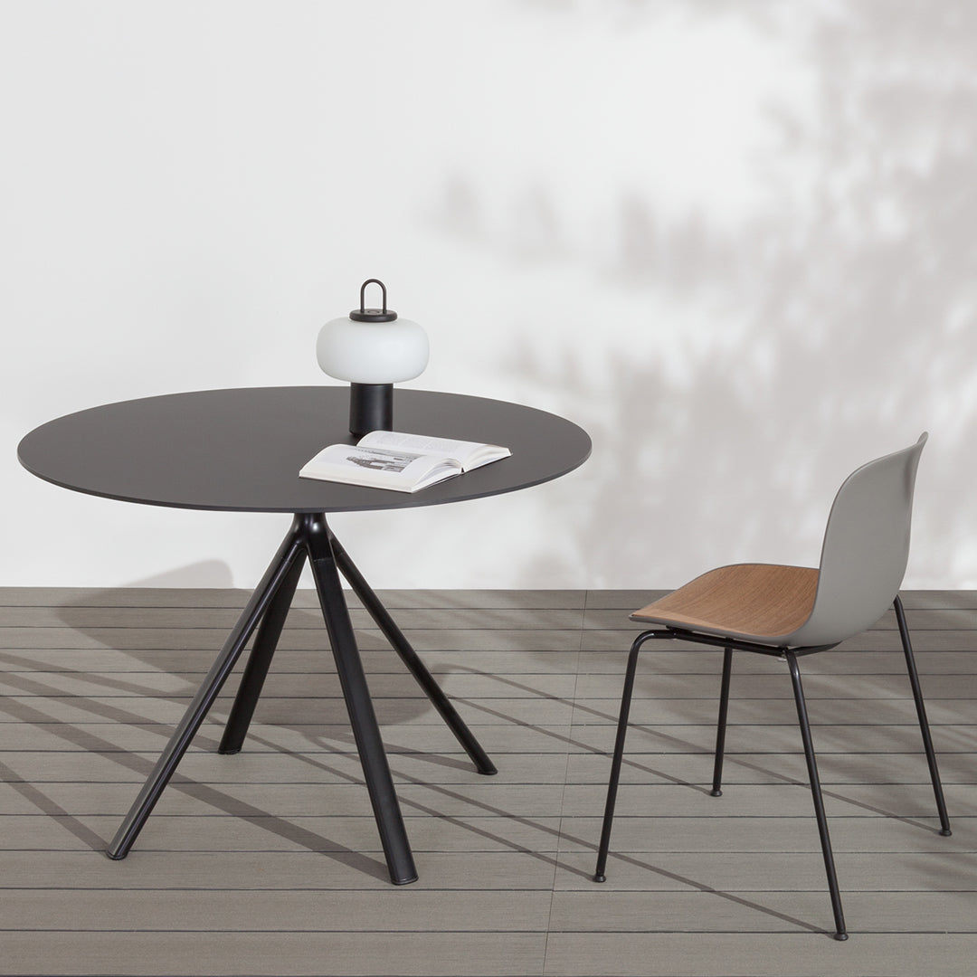 Modern round black table with a minimalist design and grey chair featuring a tan seat. Perfect for contemporary spaces.