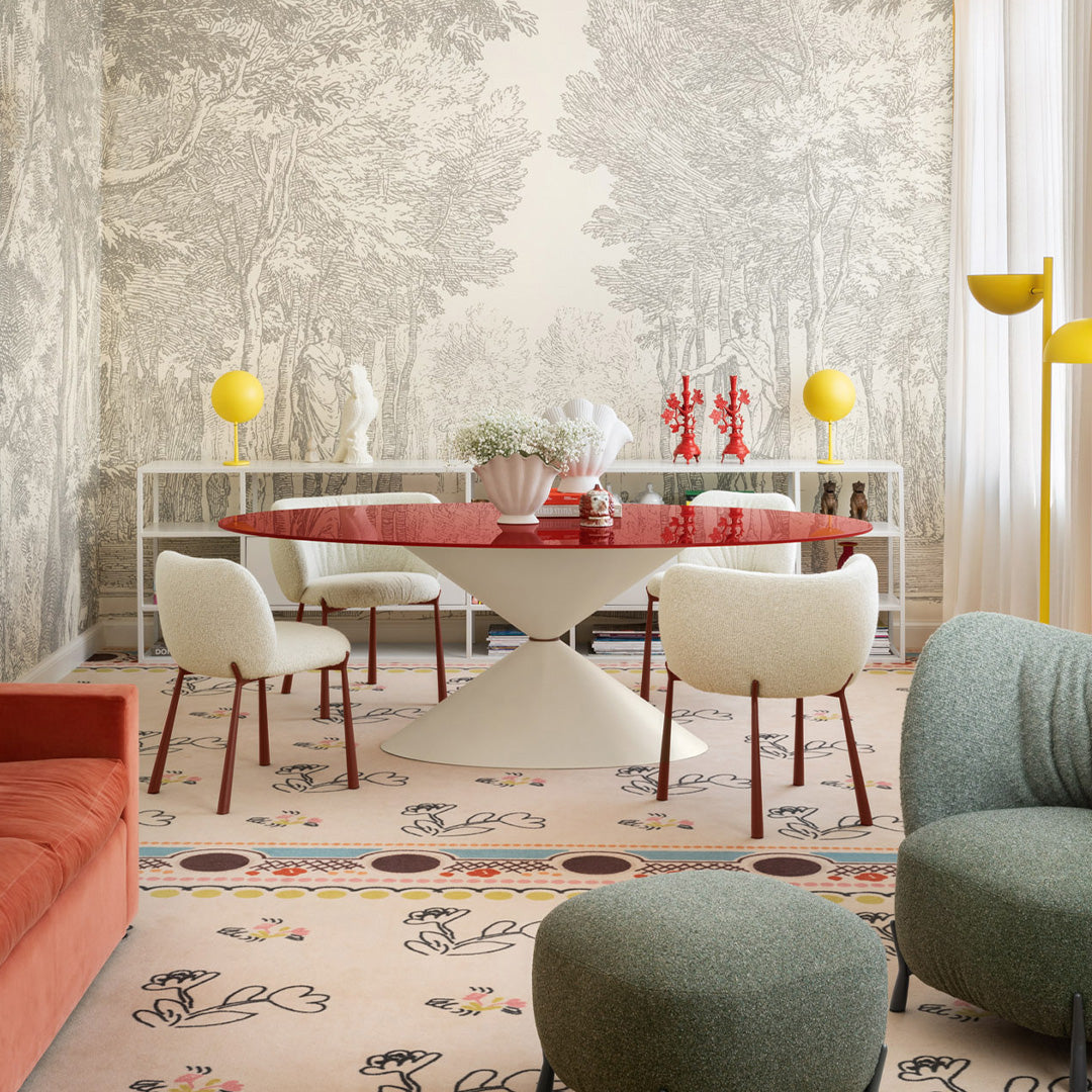 Bright red round table, soft cream chairs, pastel patterned rug, and bold yellow accents create a vibrant dining space.