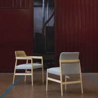 Pair of modern chairs featuring a light wood frame, soft gray and beige upholstery, set against a red backdrop.