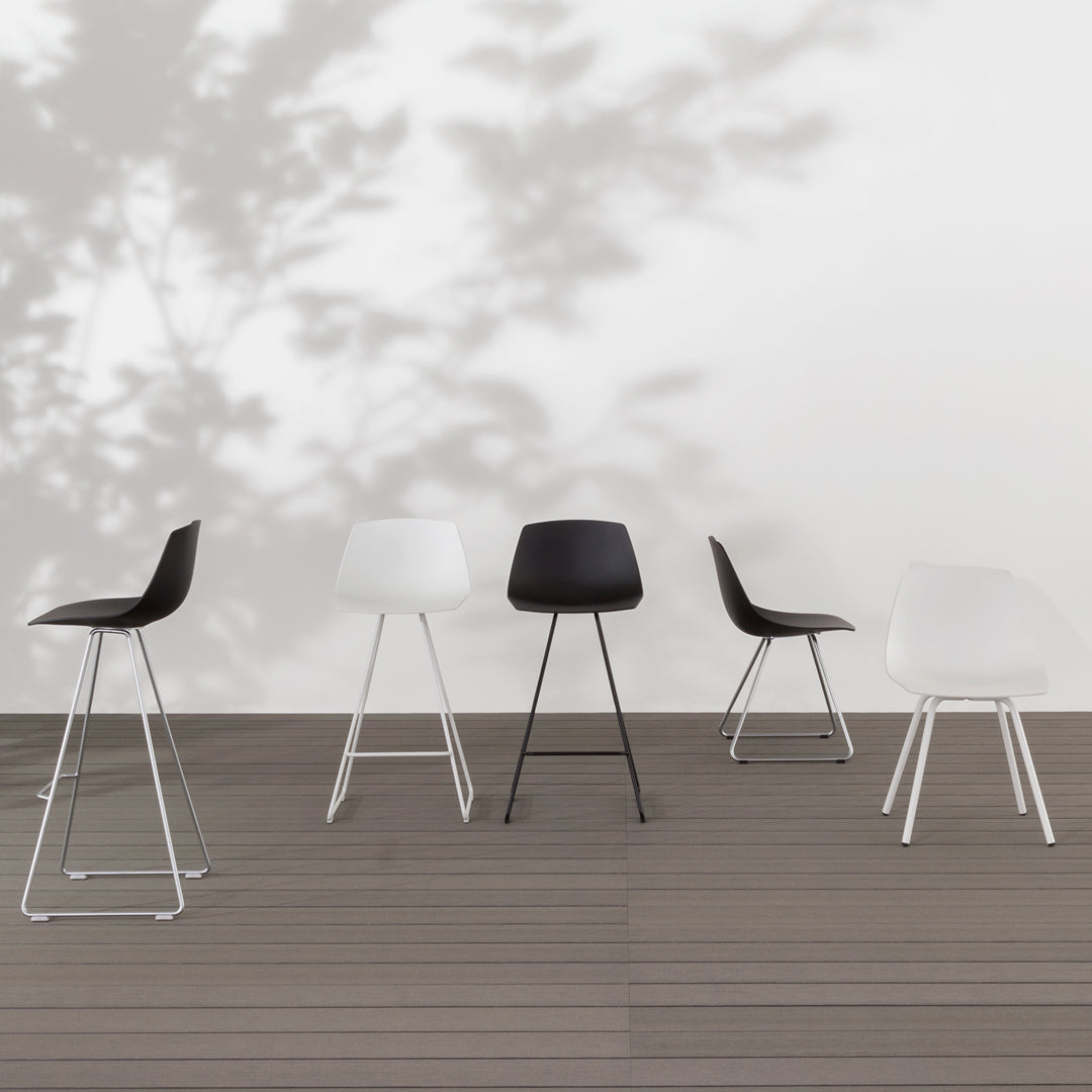 Five modern bar stools in black and white, featuring smooth finishes and minimalist designs on a wooden deck.
