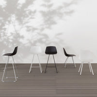 Five modern bar stools in black and white, featuring smooth finishes and minimalist designs on a wooden deck.