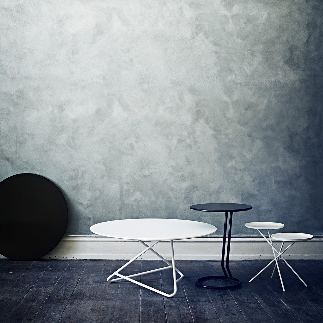 Three modern tables in black, white, and navy against a textured gray wall, showcasing sleek, minimalist design.