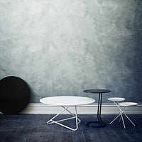 Three modern tables in black, white, and navy against a textured gray wall, showcasing sleek, minimalist design.