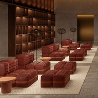 Modern sofa in rich burgundy with tan accents, set against a neutral textured rug and wood-paneled backdrop.