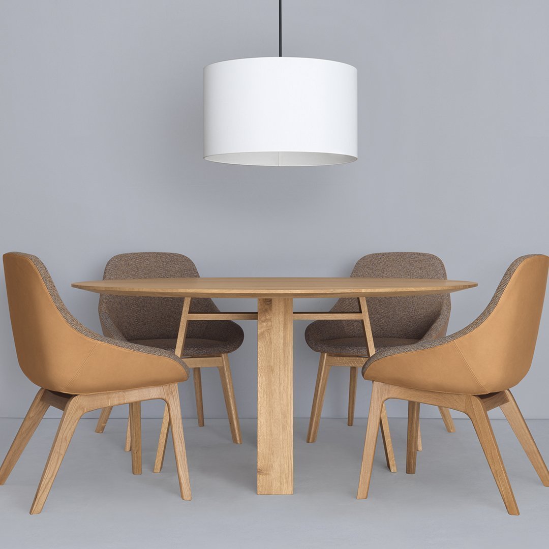 "Round wooden table with light brown and beige chairs, paired with a white pendant lamp against a gray backdrop."