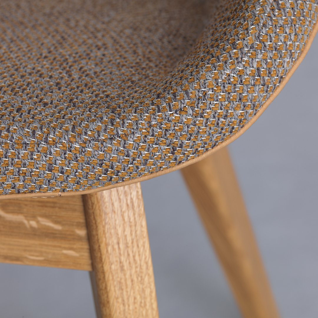 Textured fabric in gray and orange pattern on a curved chair seat, with natural wood legs.
