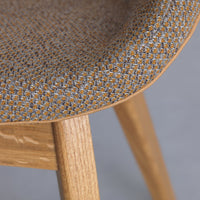 Textured fabric in gray and orange pattern on a curved chair seat, with natural wood legs.