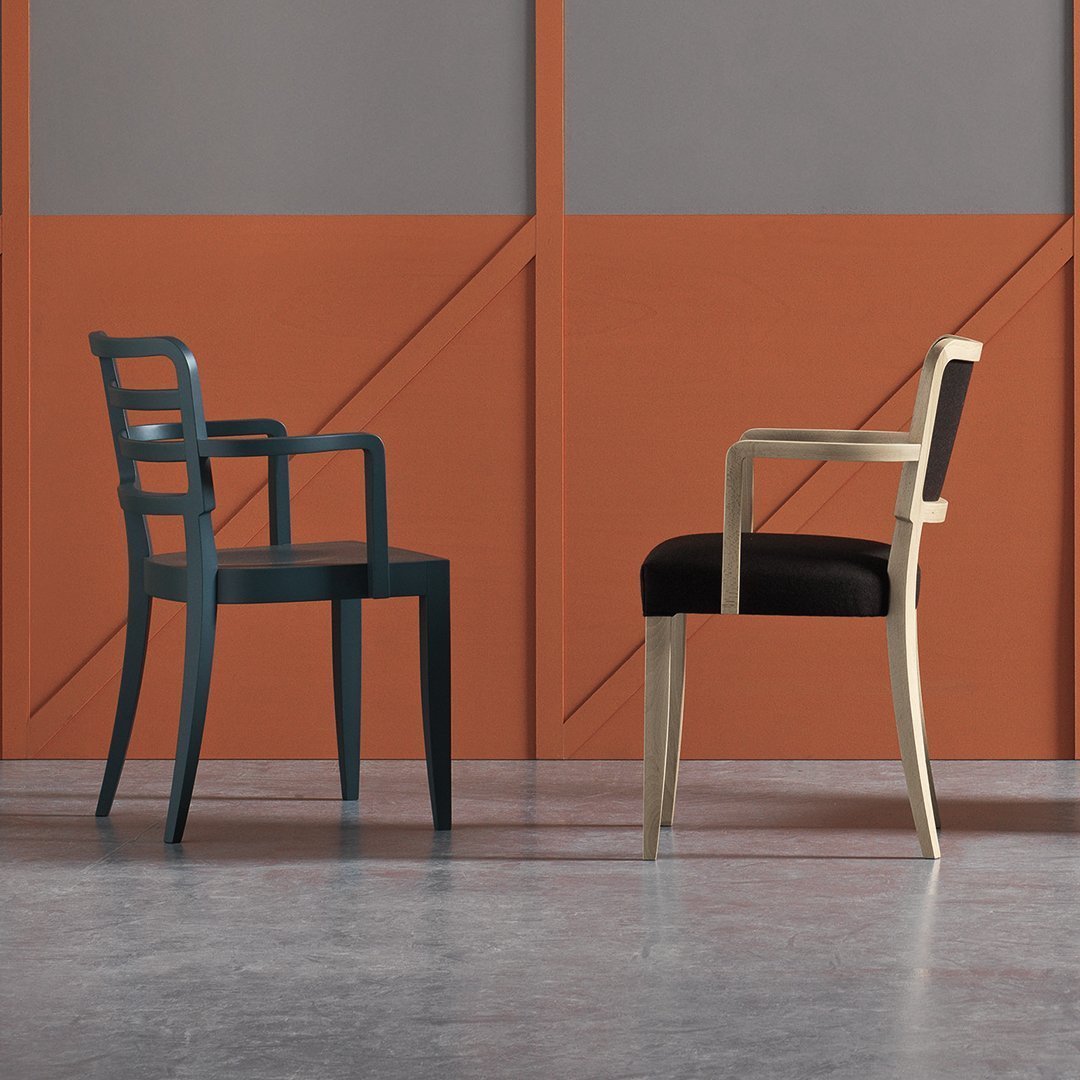Two modern chairs: one in deep blue with a slatted back, the other in light wood with a black cushion against a geometric backdrop.