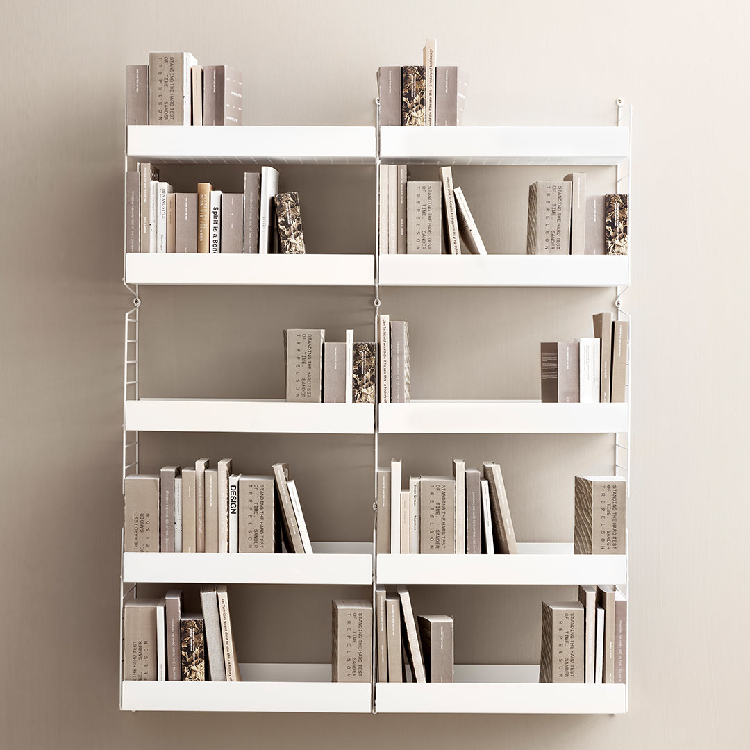 White shelving unit with horizontal shelves displaying various neutral-toned books and decorative spines.