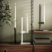 Minimalist candle holders in black, white, and gray, featuring sleek lines against a muted green backdrop.