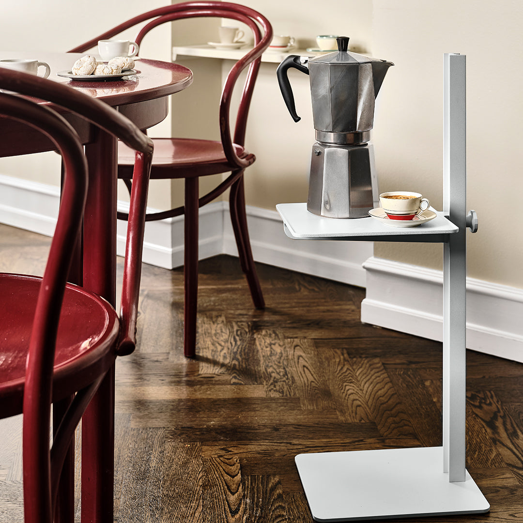 Modern gray table with a sleek white top, set against warm wooden flooring and vibrant red chairs.