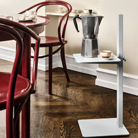 Modern gray table with a sleek white top, set against warm wooden flooring and vibrant red chairs.