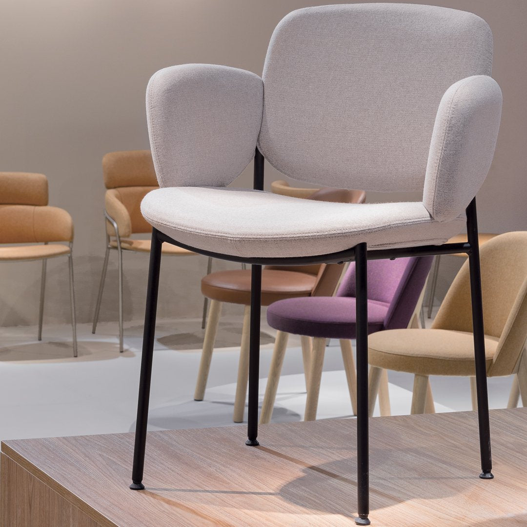 Light gray upholstered chair with soft curves, featuring a black metal frame and surrounded by pastel-colored chairs.