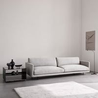Light gray sofa with sleek lines, complemented by a textured white rug and dark accent table. Modern minimalist design.