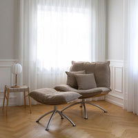 Soft beige lounge chair with textured cushions, set against light-colored walls and a warm wooden floor.