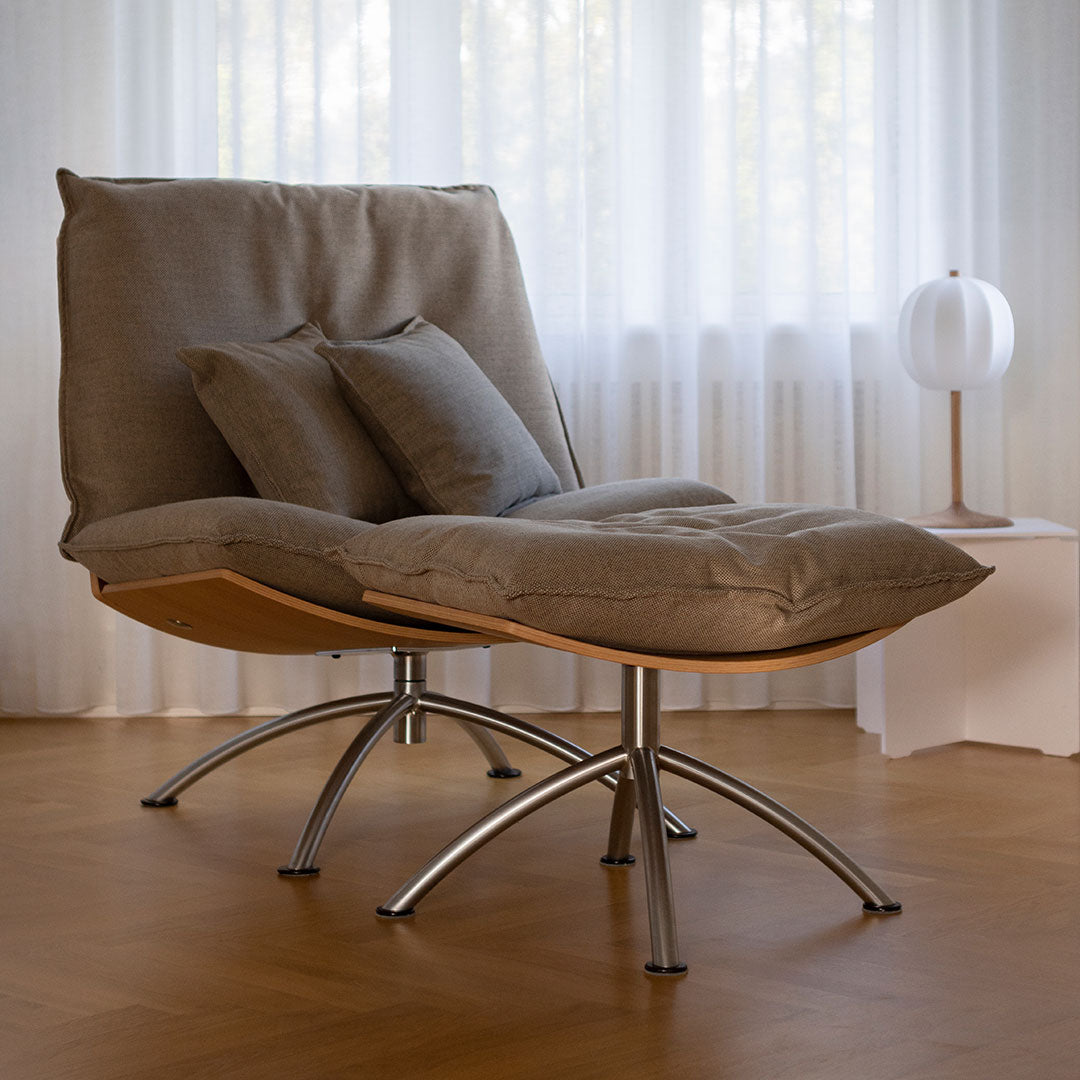 Gray lounge chair with smooth fabric, complemented by two matching cushions and sleek silver metal base.