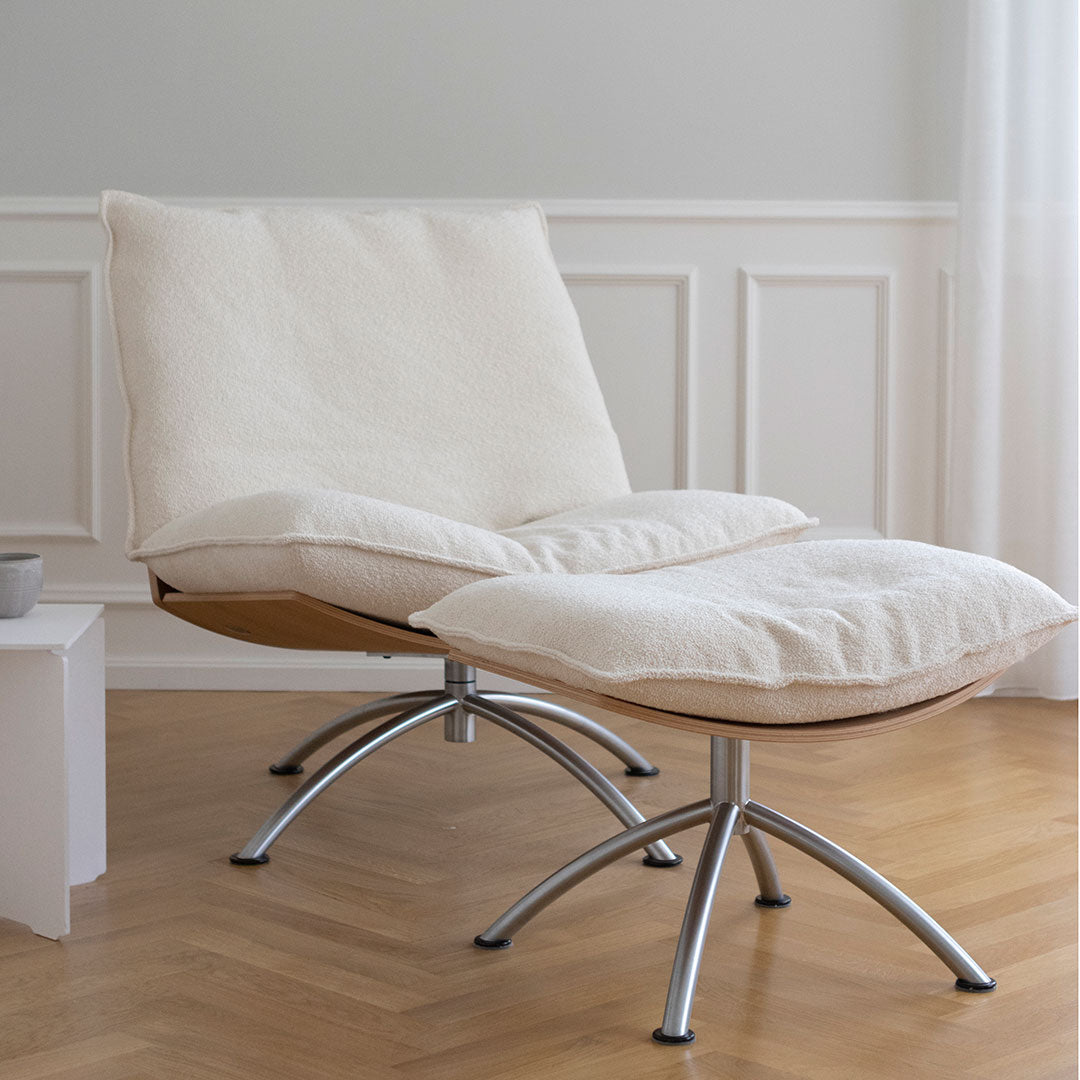 Cream upholstered lounge chair with a minimalist design and natural wood accents, resting on sleek chrome legs.