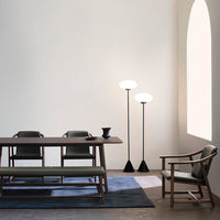 Minimalist dining room featuring neutral tones, soft green upholstery, and dark geometric lamp designs.