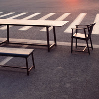 Modern black table and bench with simple lines, set against a faded asphalt background and subtle sunset hues.