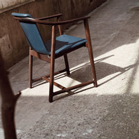 Wooden chair with a dark brown frame and deep blue upholstery, set on a textured concrete surface.