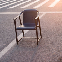 Blue upholstered chair with a sleek black frame, set against a textured asphalt background and striped white lines.
