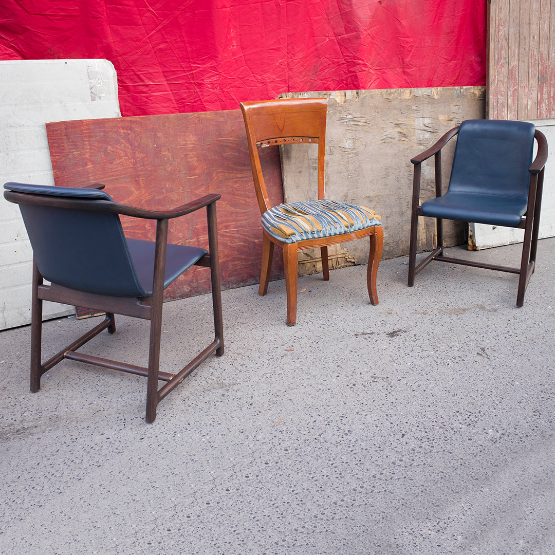 "Three vintage chairs: two dark blue with wood frames and one patterned seat with orange, yellow, and blue stripes."
