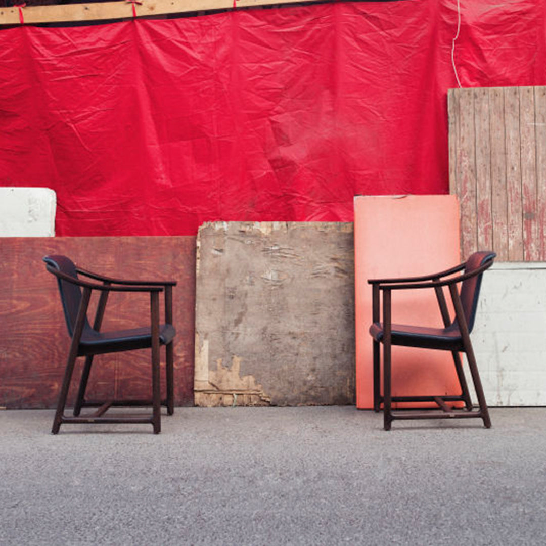 "Two black chairs against a vibrant red backdrop with assorted wooden panels in neutral tones."