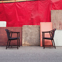 "Two black chairs against a vibrant red backdrop with assorted wooden panels in neutral tones."