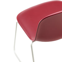 Red curved chair with a smooth surface and sleek white metal legs, showcasing a modern design.
