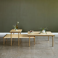 "Set of three minimalist coffee tables in natural wood with gold accents, against a textured green wall."