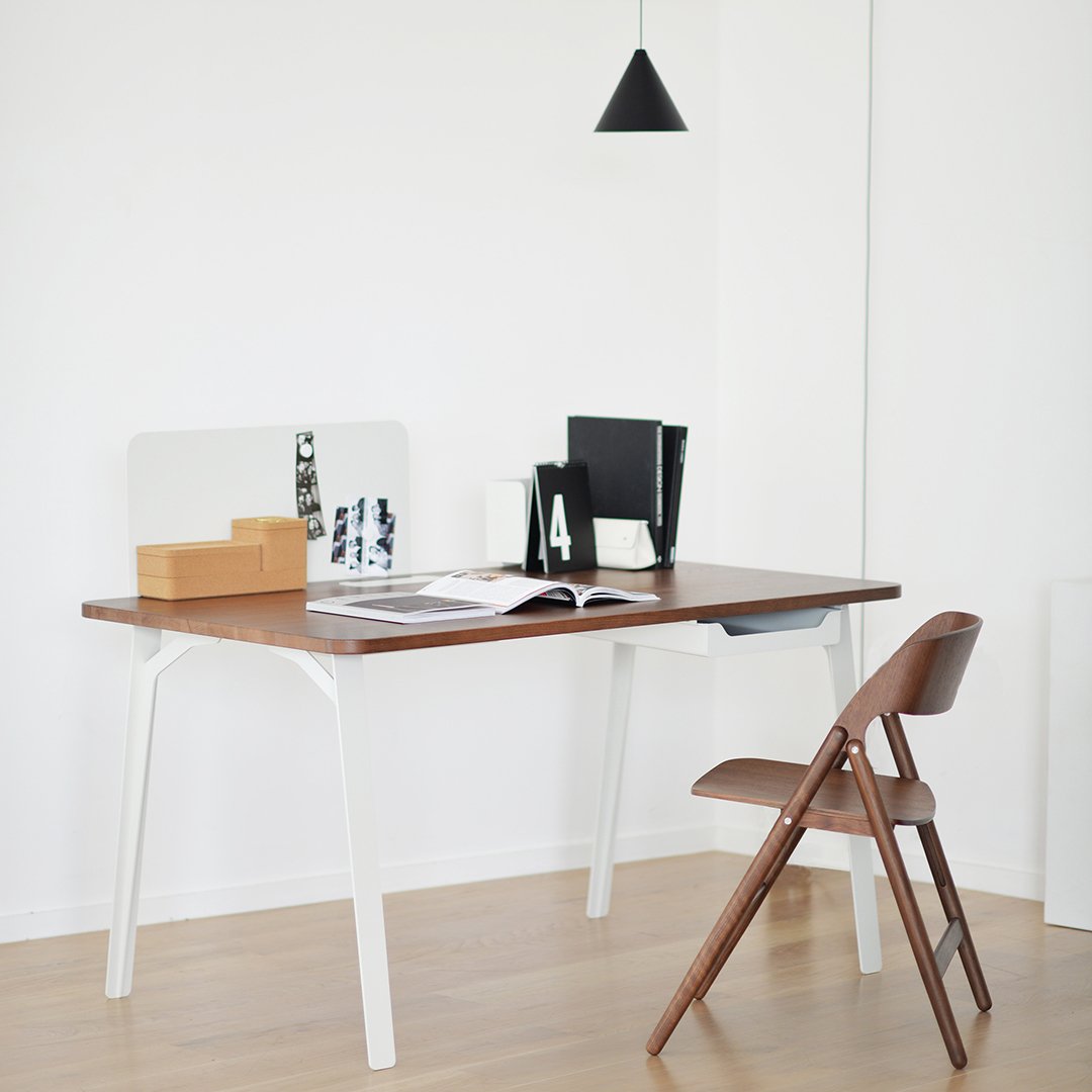 Modern brown wooden desk with white legs, complemented by a minimalist brown folding chair, in a bright, clean workspace.