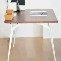 Modern wooden desk with a walnut finish and sleek white legs, featuring minimalistic design and clean lines.
