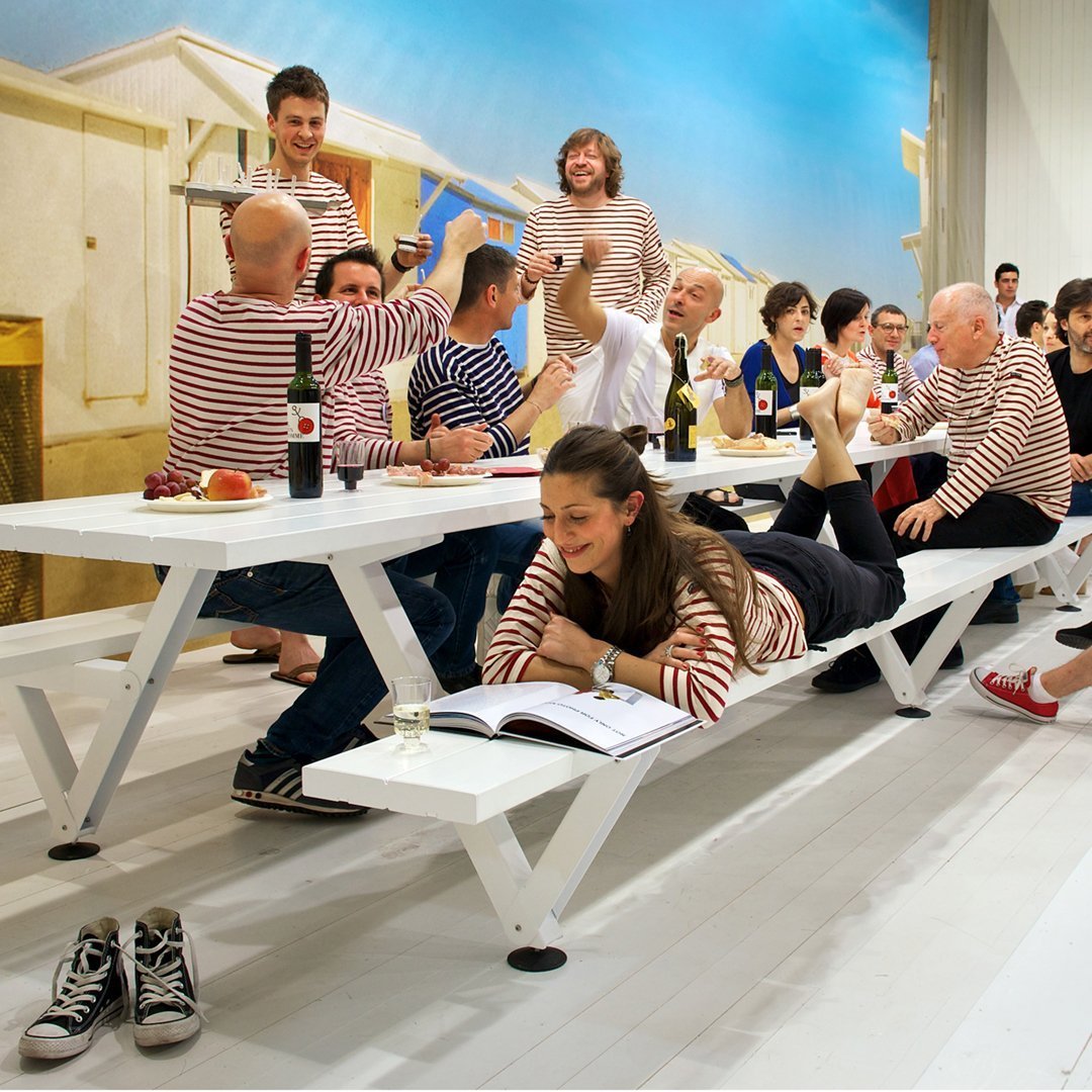 "Casual dining scene featuring white tables and blue stripes, with attendees in red and white striped attire."