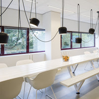 Modern white dining table with sleek black pendant lights and neutral gray flooring. Minimalist design aesthetic.