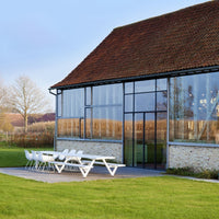 Modern glass building with a brown roof, white outdoor furniture, and green grass, set against a clear blue sky.