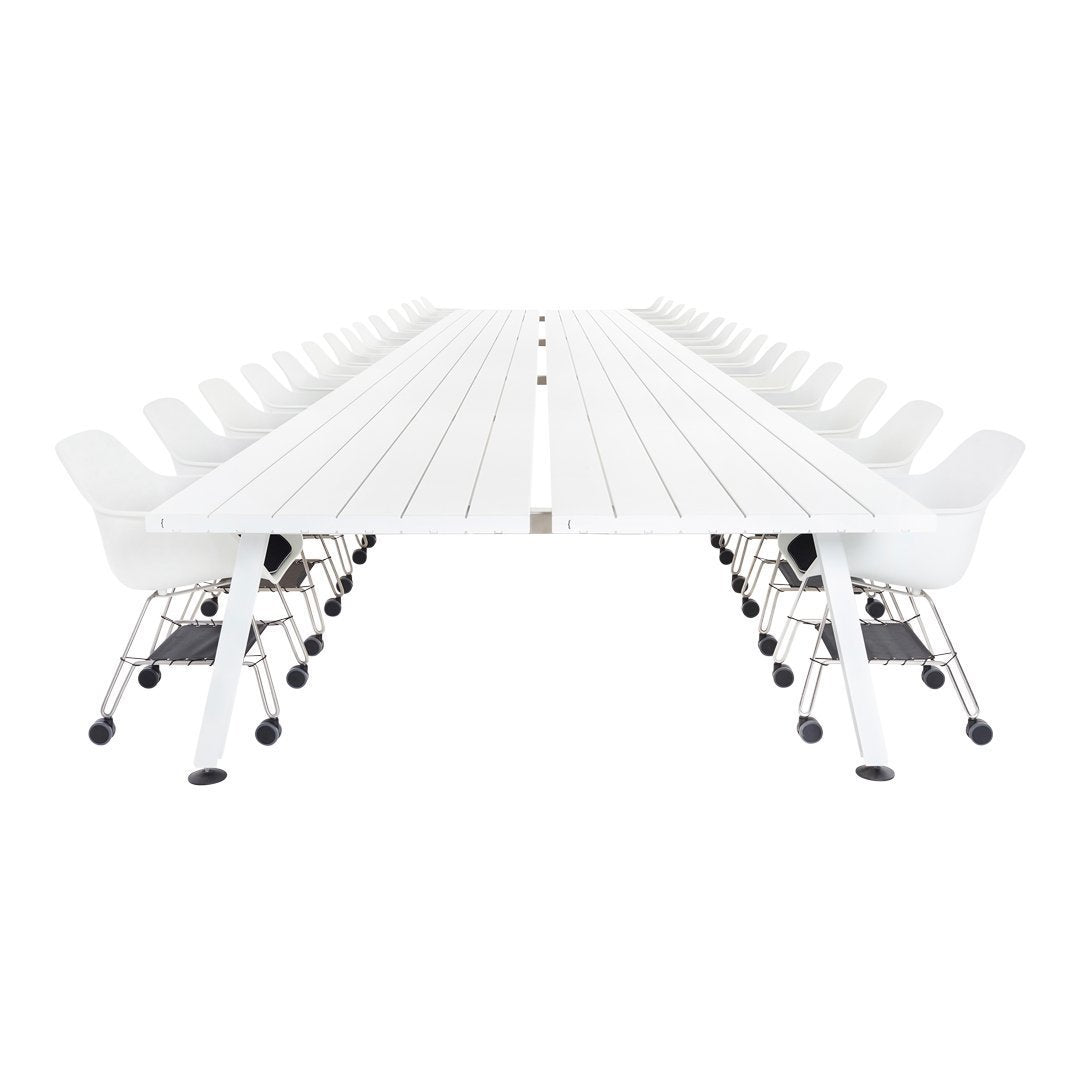 Long white table with a smooth surface and minimalist design, featuring curved white chairs on chrome wheels.