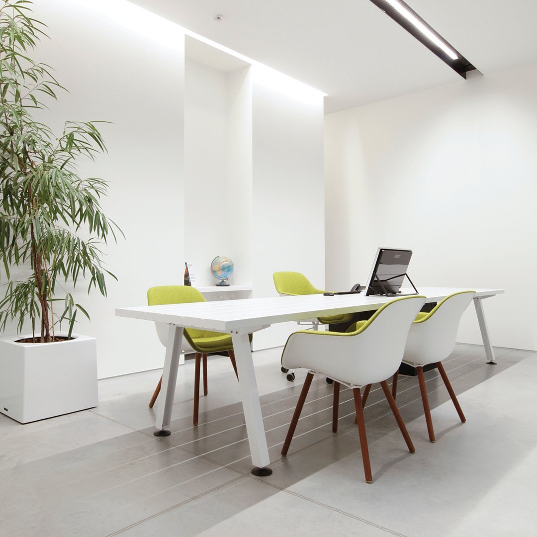 Modern white office table with green chairs, featuring sleek lines and minimalistic design against a bright, neutral backdrop.