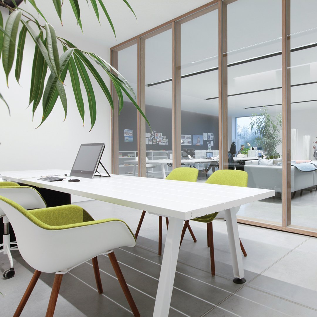 Modern office with a sleek white table, light wood accents, and vibrant green chairs in a minimalist design.