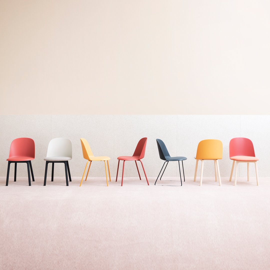 "Colorful modern chairs in red, yellow, black, white, and orange arranged against a soft pink backdrop."
