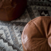 Brown leather poufs on a geometric gray and black patterned rug, showcasing rich textures and warm hues.