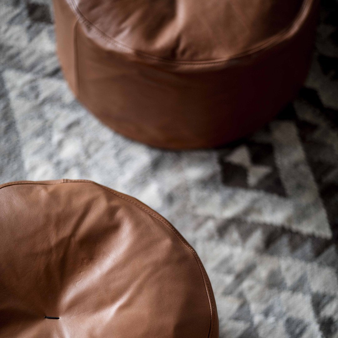 Brown leather poufs on a geometric patterned gray and white rug. Modern and stylish home decor accents.