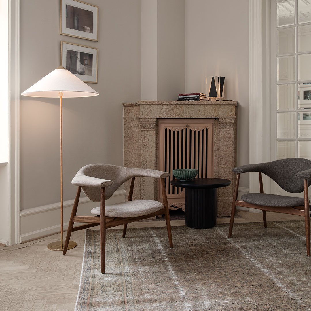 Cozy living room with neutral beige and gray chairs, a black side table, and a light wood floor featuring subtle patterns.