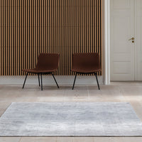 Gray area rug with a soft, textured finish, complementing a room with brown striped wall and minimalist chairs.