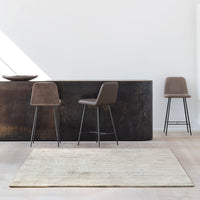 Brown upholstered bar stools with sleek black metal legs against a light, neutral-colored rug and a dark wooden counter.