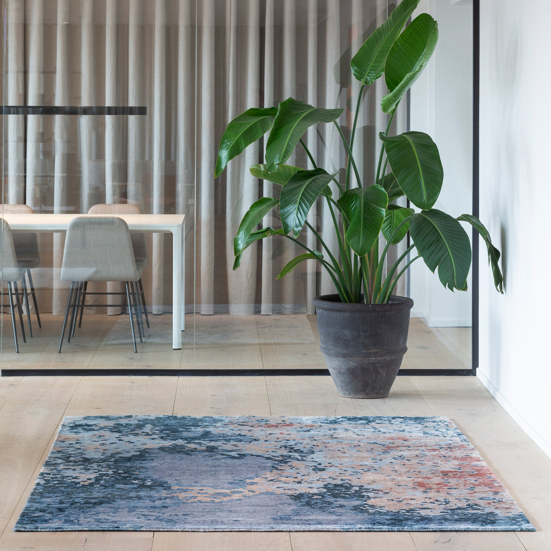 Multi-colored abstract rug with blue, gray, and hints of warm tones, featuring intricate patterns and textures.