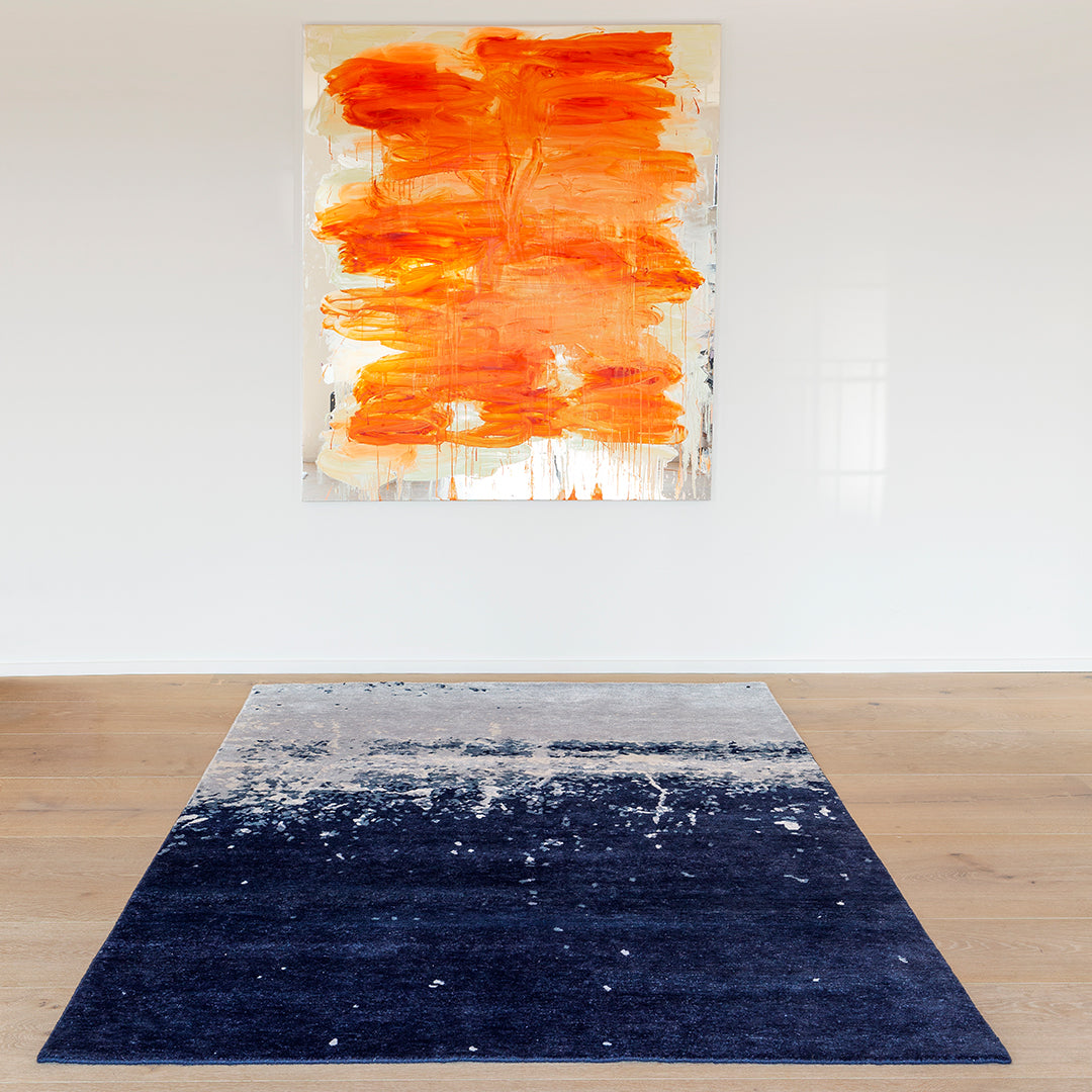 Navy blue rug with an abstract white and gray pattern, complementing an orange and white artwork above.
